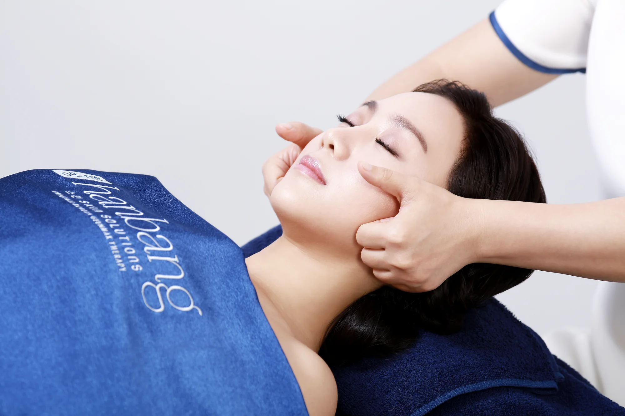 A Hanbang therapist applying Geunmak therapy along a client's cheekbones