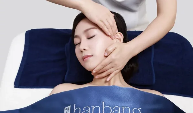 A therapist's hands lifting along a client's jaw and temple during a Hanbang facial